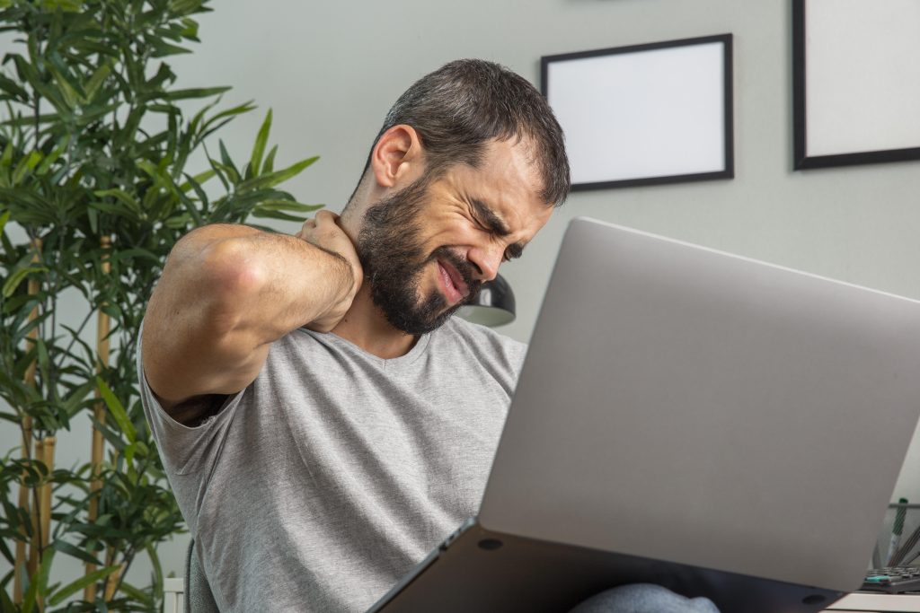 homem com dor no pescoco enquanto trabalha em casa usando um laptop
